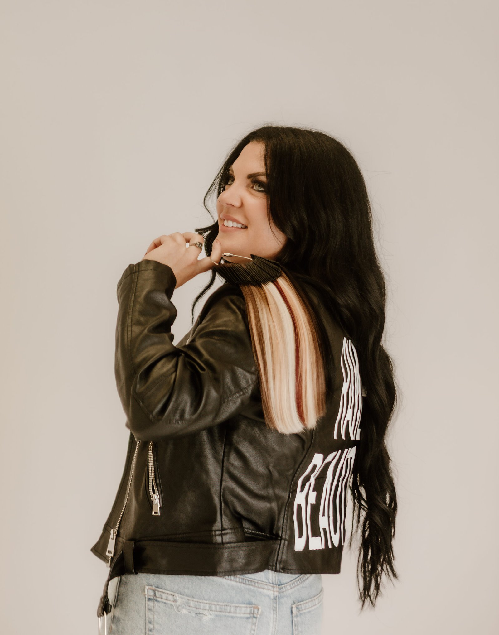 A picture of Morgan, owner of Rawe beauty. She has long lback hair and is standing with her back to the camera holding hair extensions in her hand.