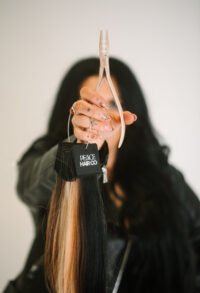 EA7A5794-2 Picture of a dark-haired woman holding out a handful of hair extensions, which are a variety of colors, including blonde and black