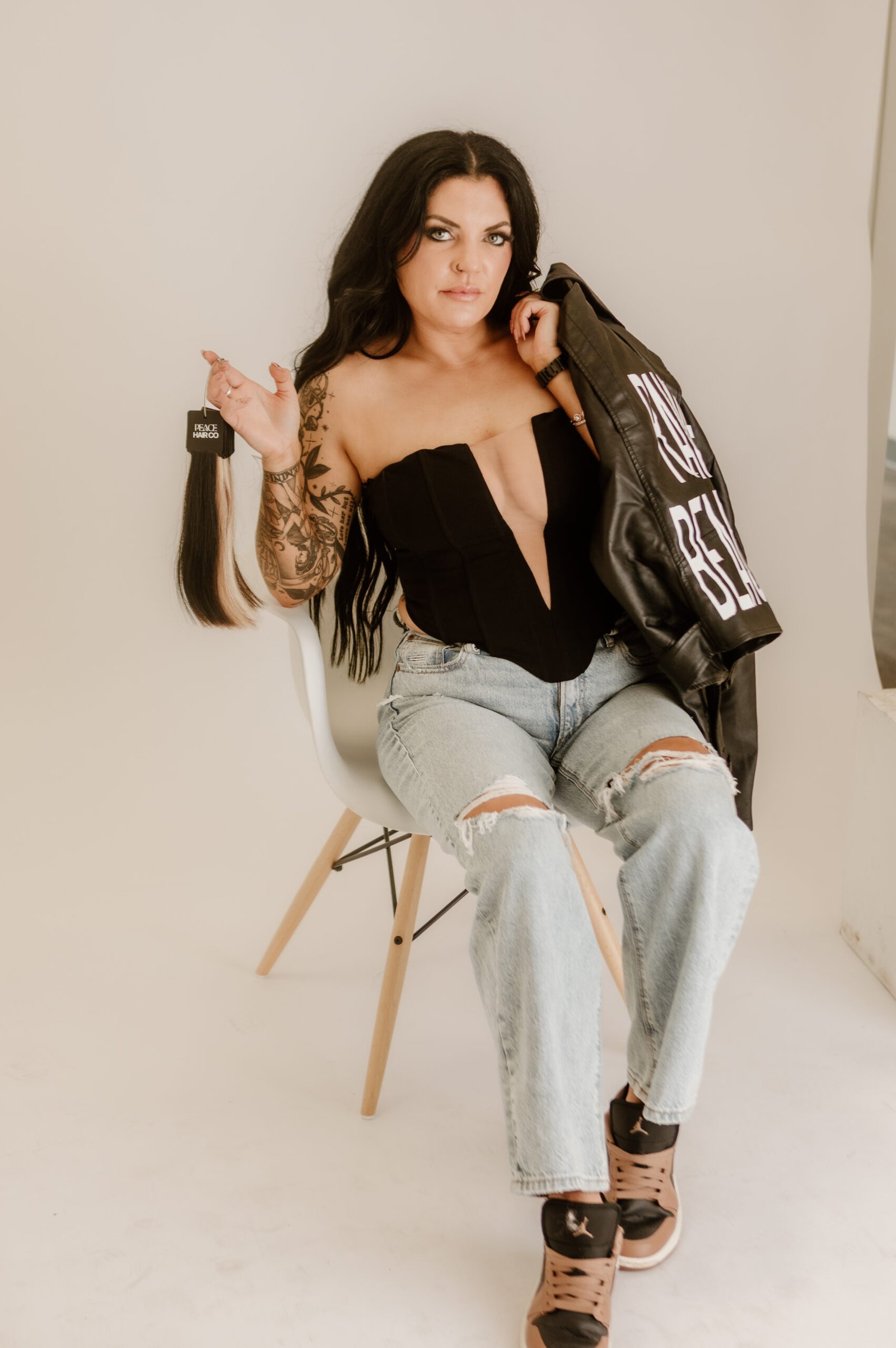 EA7A5861 A picture of Morgane Rowe, a brunette woman with long hair, sitting in a chair holding hair extensions in one hand