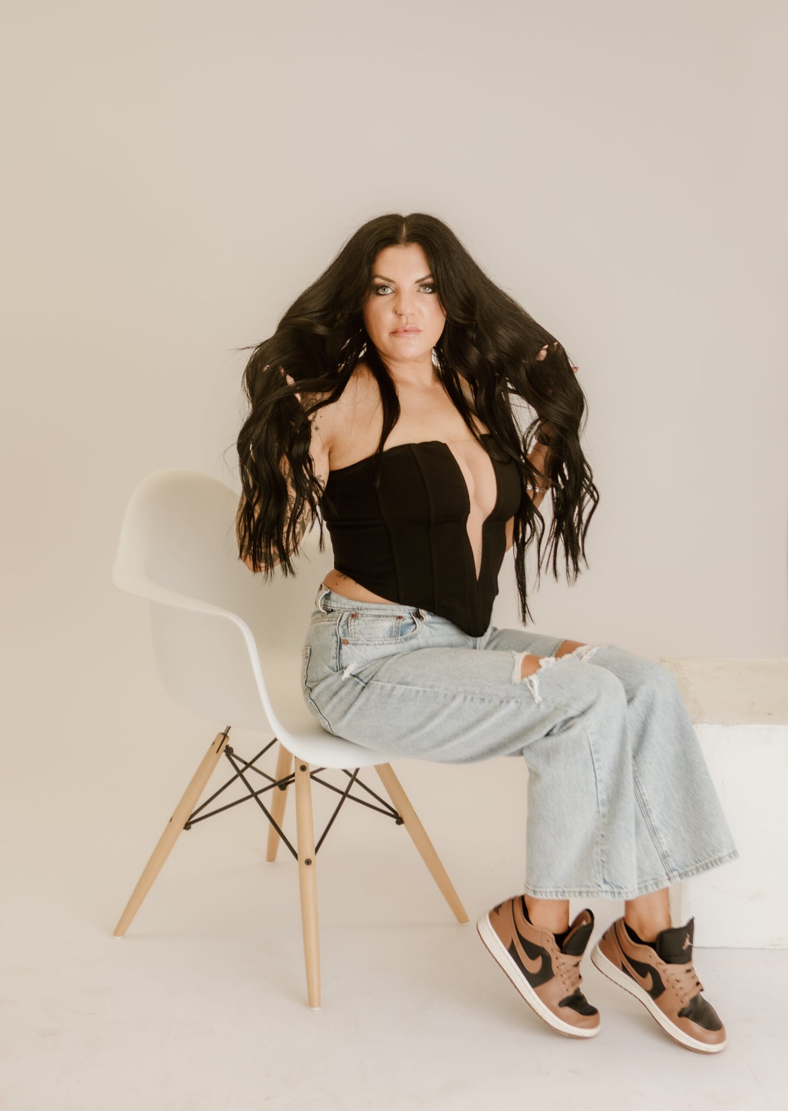 EA7A5897 A picture of Morgane Rowe, a brunette woman with long hair, sitting in a chair holding hair extensions in one hand